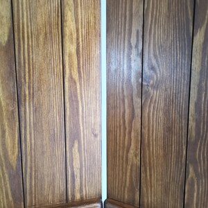 May include: Two wooden panels with a vertical grain pattern. The panels are joined together with a thin white space between them. The panels are a dark brown color.