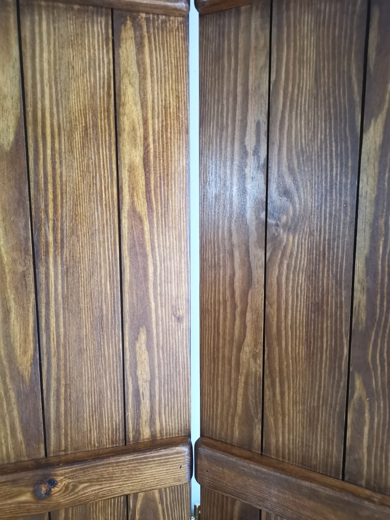 May include: Two wooden panels with a vertical grain pattern. The panels are joined together with a thin white space between them. The panels are a dark brown color.