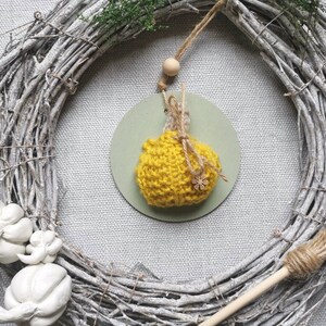 Pu&ograve; includere: Un ornamento a forma di zucca in crochet giallo appeso a una ghirlanda di rami con una piccola perla di legno e uno spago. La ghirlanda &egrave; fatta di rami bianchi e ha una scopa di iuta appoggiata ad essa.