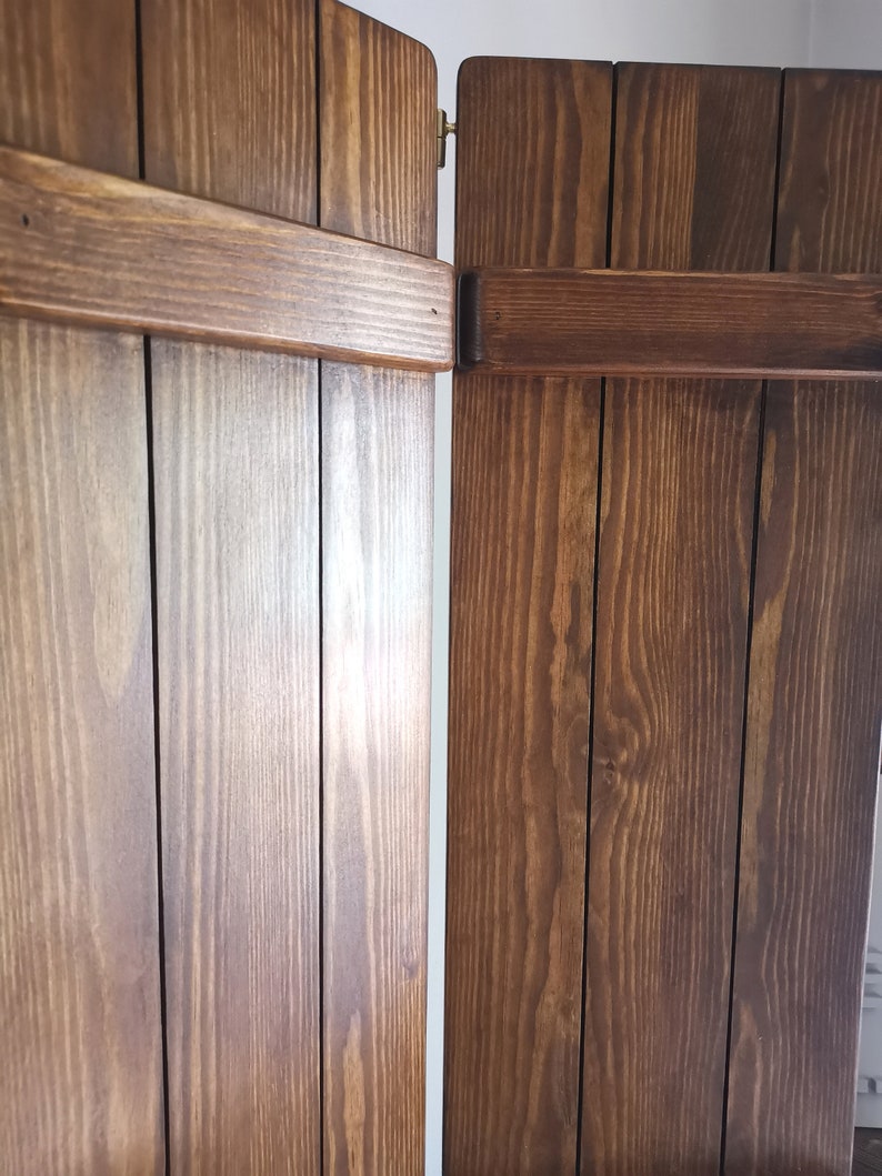 May include: Two wooden shutters, each with four vertical panels, are closed and hinged together. The shutters are a dark brown color with a natural wood grain pattern.