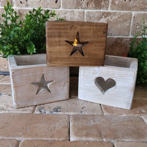 May include: Three wooden candle holders with different cutout designs. The first holder is brown with a star cutout, the second is white with a star cutout, and the third is white with a heart cutout.