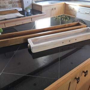 Op de afbeelding: Twee houten trays, een van naturel hout en een witgeschilderd, met een sterrendesign. De trays staan op een zwart aanrecht.