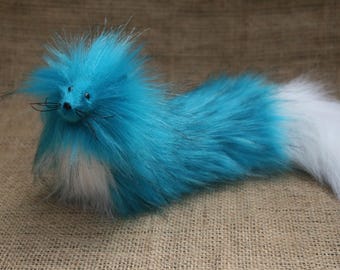May include: A whimsical, plush creature with a fluffy, turquoise body and a white tail. The toy has a small face with whiskers and is set against a neutral background.