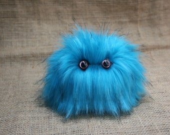 May include: A fluffy blue and black creature with large, sparkly eyes. The creature is made of soft fur and has a round, cuddly shape.