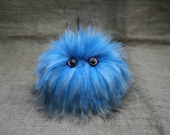 May include: A blue and white fluffy toy with black accents and large pink eyes.