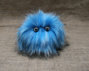 May include: A blue and white fluffy toy with black eyes. The toy is shaped like a ball and has a soft, fuzzy texture.