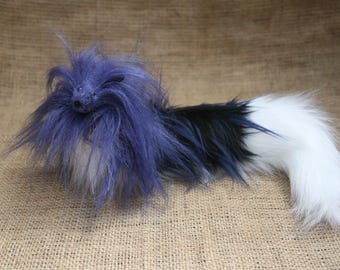 May include: A fluffy, handmade toy dog with blue, black, and white fur. The toy is lying on a brown burlap surface.