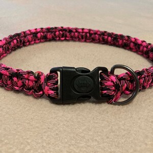 May include: A pink and black camouflage dog collar with a black plastic buckle and a silver metal D-ring.