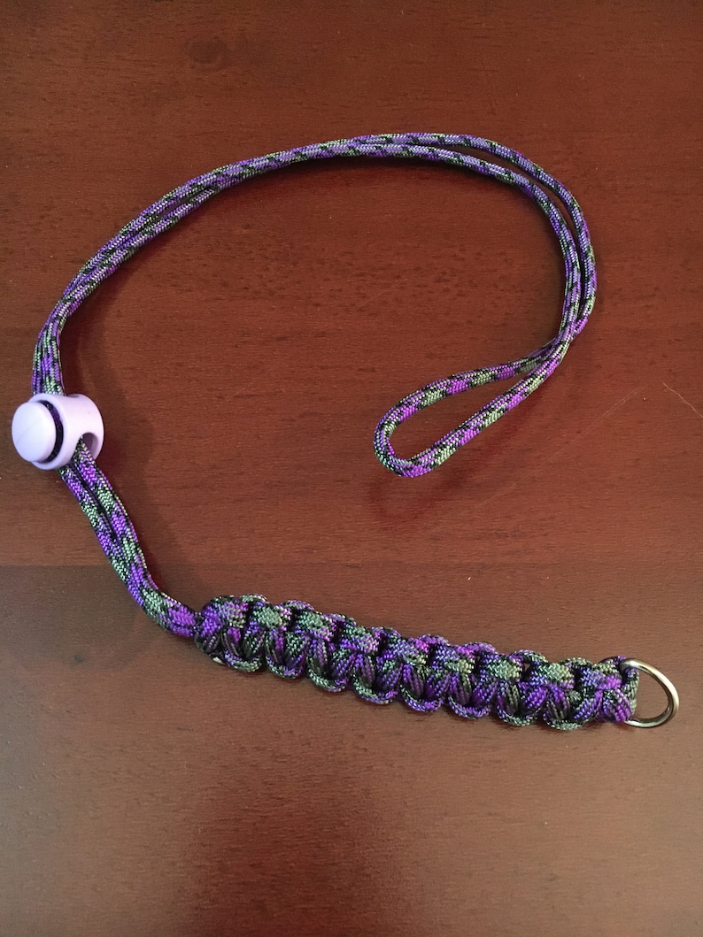 May include: A purple and green camouflage lanyard with a white plastic bead and a silver metal ring.