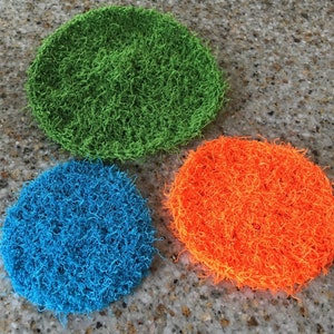 May include: Three round, crocheted scrubbers in green, blue, and orange. The scrubbers are made of a soft, fluffy material and are perfect for cleaning dishes or other surfaces.