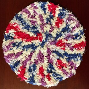 May include: A round, crocheted potholder with a spiral pattern in shades of red, white, blue, and purple.