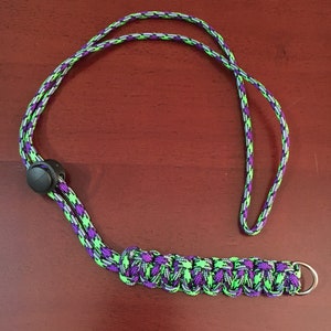 May include: A green and purple lanyard with a black plastic clip and a silver metal ring. The lanyard is made of braided cord.
