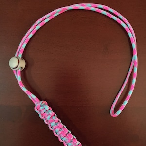 May include: A pink and blue paracord lanyard with a white bead and a silver ring at the end.