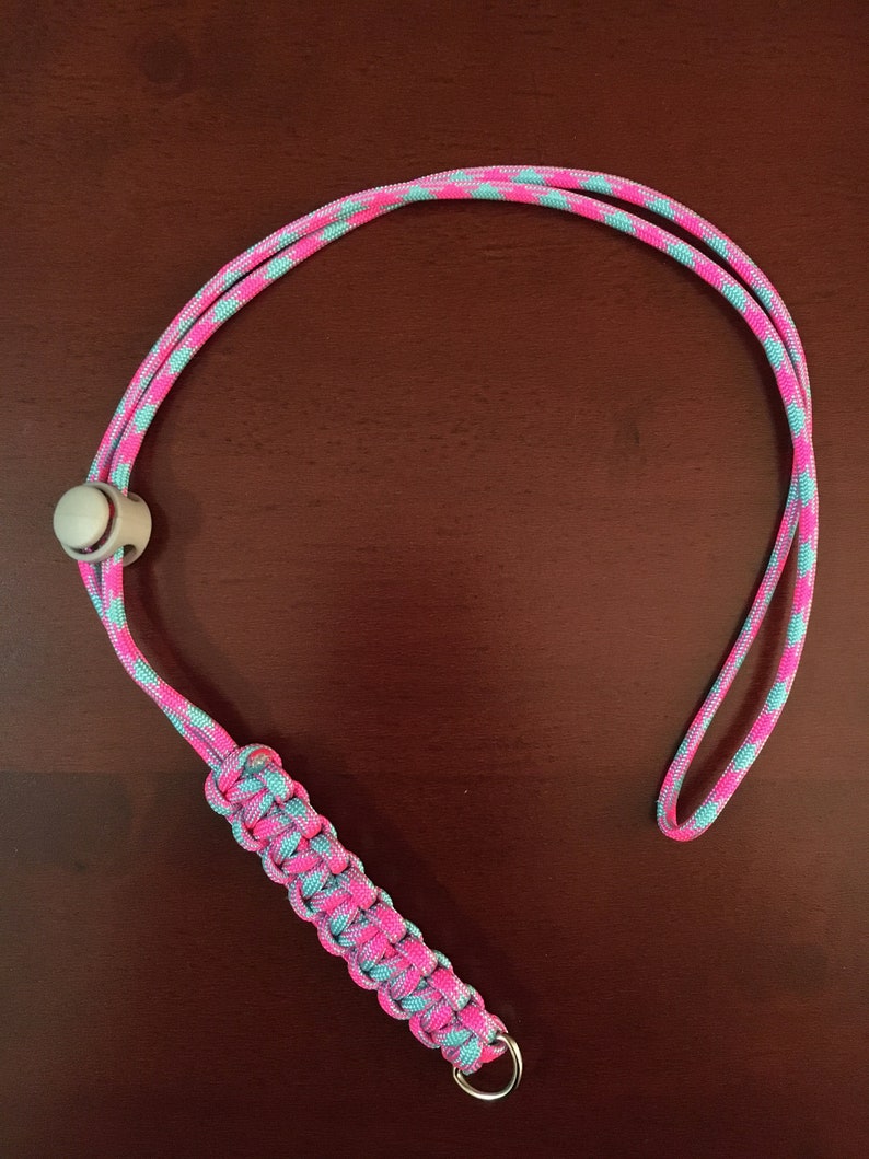 May include: A pink and blue paracord lanyard with a white bead and a silver ring at the end.