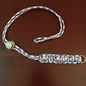 May include: A purple, pink, and blue paracord lanyard with a white plastic bead and a silver metal ring.