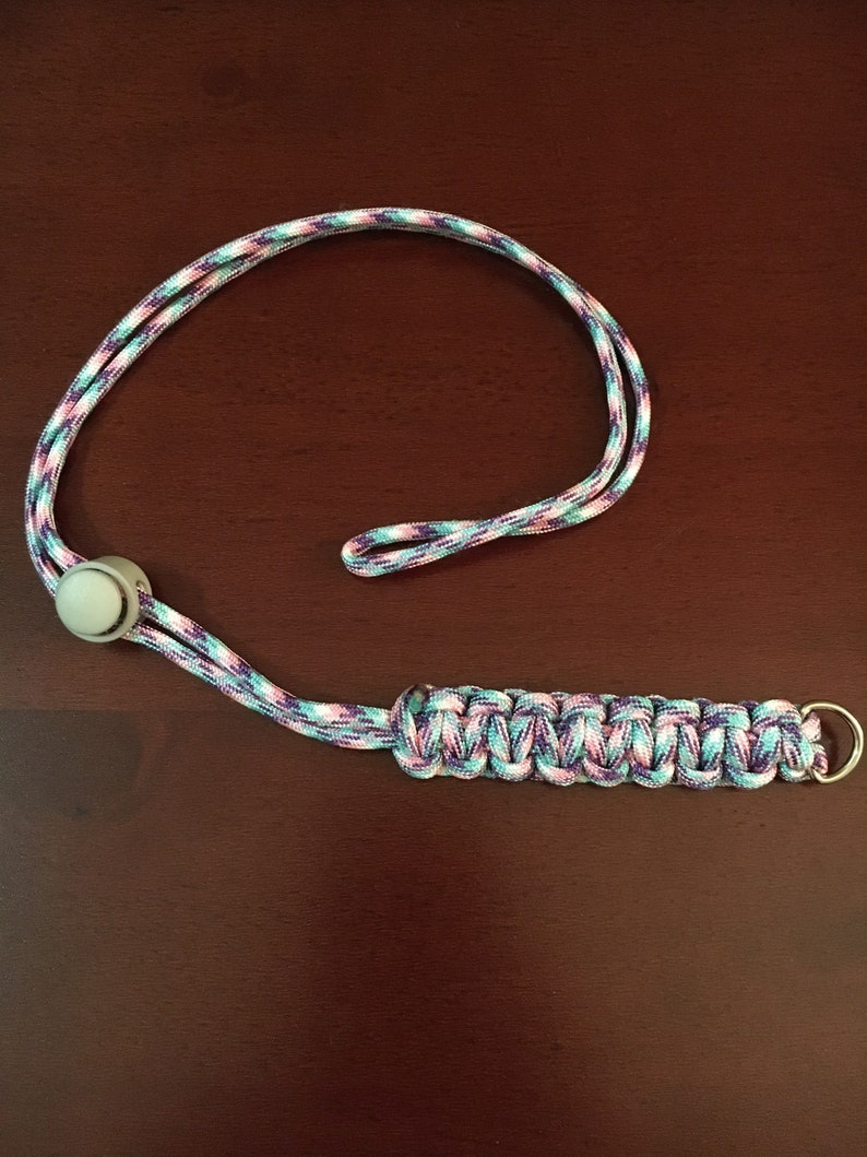 May include: A purple, pink, and blue paracord lanyard with a white plastic bead and a silver metal ring.