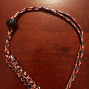 May include: A black and orange paracord lanyard with a black plastic clip and a silver metal ring.