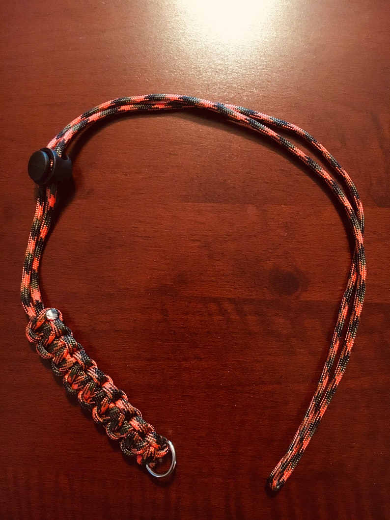 May include: A black and orange paracord lanyard with a black plastic clip and a silver metal ring.