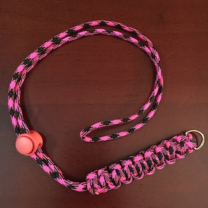 May include: A pink and black paracord lanyard with a pink plastic toggle and a silver metal ring.