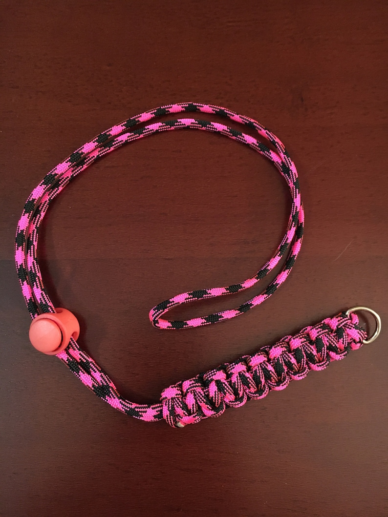 May include: A pink and black paracord lanyard with a pink plastic toggle and a silver metal ring.