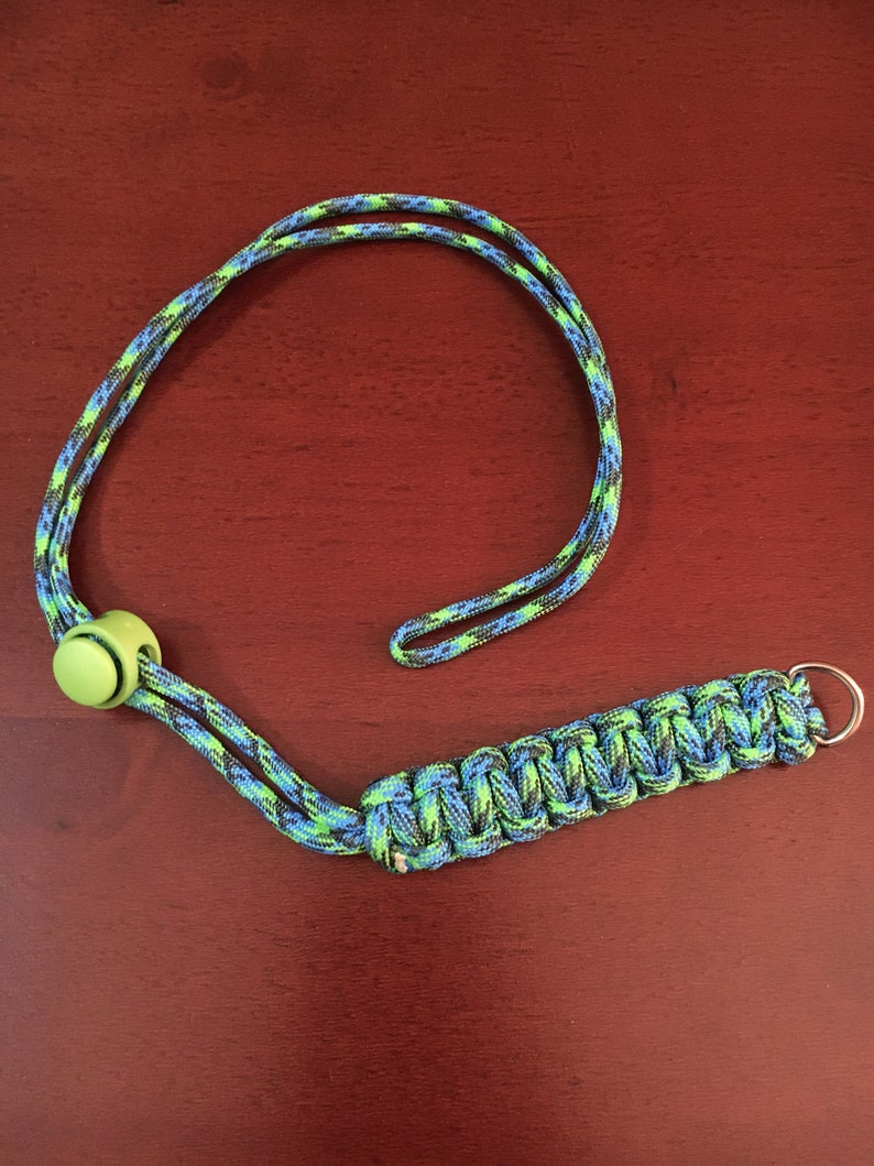 May include: A green, blue, and black paracord lanyard with a green plastic toggle and a silver metal ring.