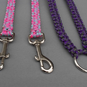 Op de afbeelding: Drie paracord-riemen met zilveren metalen gespen. Eén riem is roze en blauw, één is turquoise en roze en één is paars en grijs.