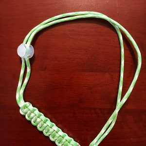 May include: A green and white striped lanyard with a white plastic toggle and a silver metal ring.