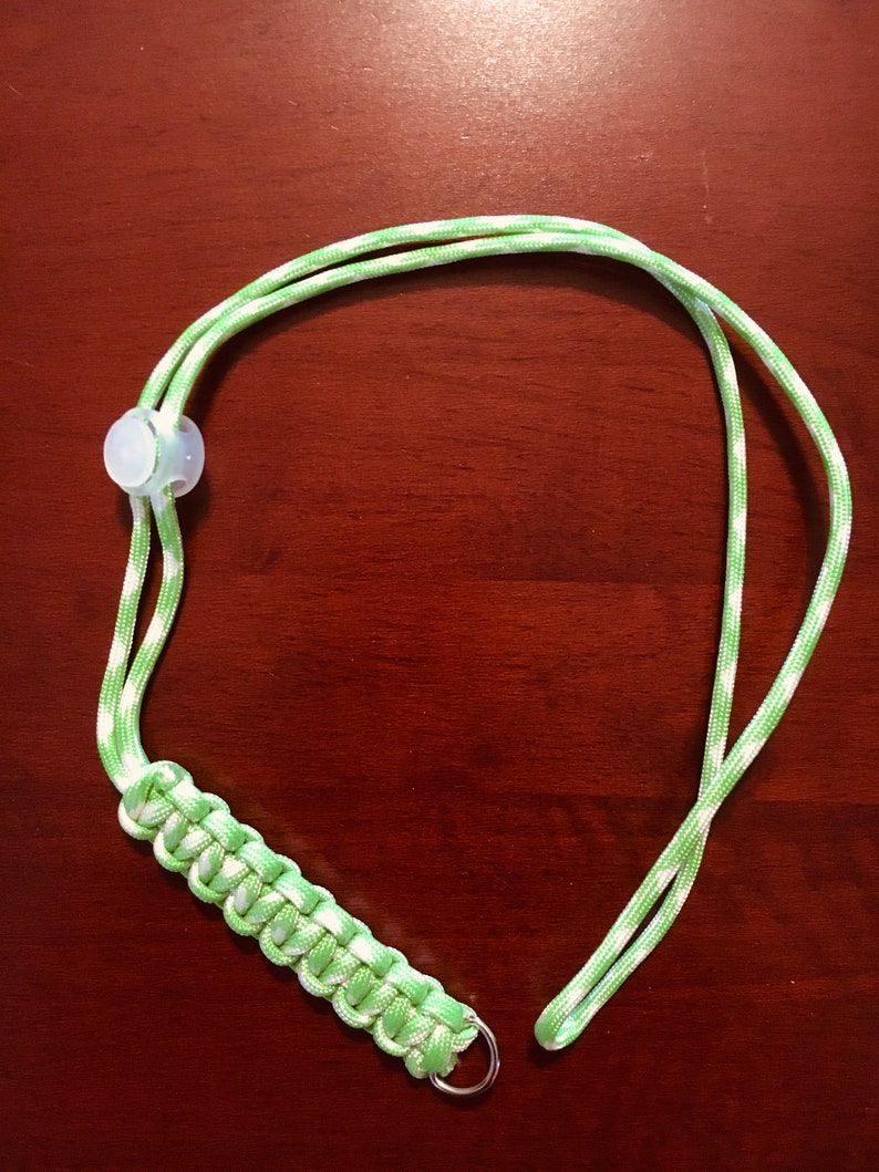 May include: A green and white striped lanyard with a white plastic toggle and a silver metal ring.