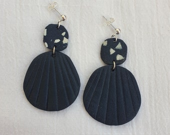May include: A pair of black and white shell-shaped earrings with a geometric pattern. The earrings are made of polymer clay and have a matte finish.