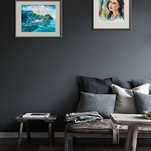 Pode incluir: Duas pinturas emolduradas em uma parede cinza escura. A pintura &agrave; esquerda representa um veleiro em um corpo de &aacute;gua com montanhas ao fundo. A pintura &agrave; direita representa uma mulher com uma flor no cabelo.