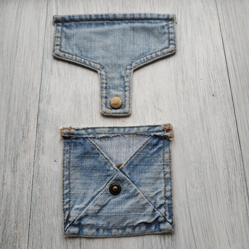May include: Two denim pockets with a button closure. The top pocket is a simple rectangle shape, while the bottom pocket is a square shape with a diagonal seam.