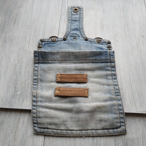 May include: A light blue denim pouch with two brown leather labels. The pouch has a flap with a snap closure and is decorated with metal rivets.