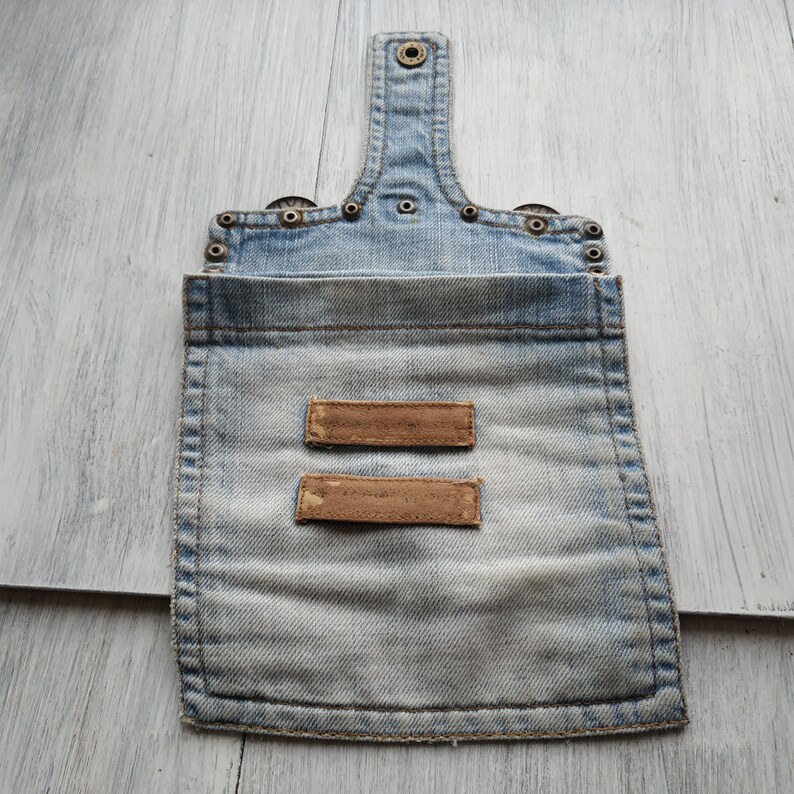 May include: A light blue denim pouch with two brown leather labels. The pouch has a flap with a snap closure and is decorated with metal rivets.