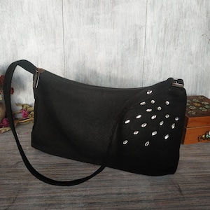 Könnte beinhalten: Eine schwarze Schultertasche mit silbernem Nieten-Design. Die Tasche hat einen Reißverschluss und einen langen Riemen.
