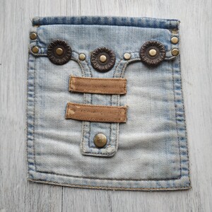 May include: A light blue denim pouch with two brown leather straps and three decorative metal buttons. The pouch has a flap with a button closure.