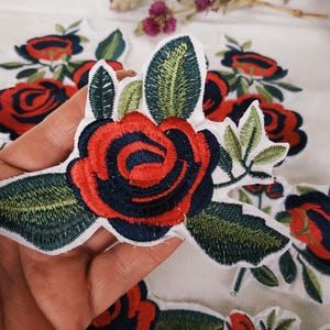 Peut inclure: Un ensemble de patchs brodés thermocollants rouges et bleus représentant des roses avec des feuilles vertes.