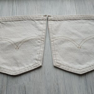 May include: Two off-white denim pockets with a contrasting brown stitch detail. The pockets are sewn together at the top.