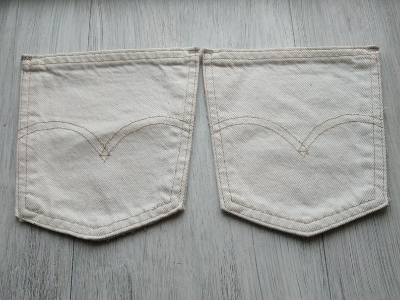 May include: Two off-white denim pockets with a contrasting brown stitch detail. The pockets are sewn together at the top.