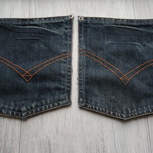 May include: Two dark blue denim pockets with brown stitching. The pockets have a diamond shape in the center and are sewn with a decorative stitch around the edges.