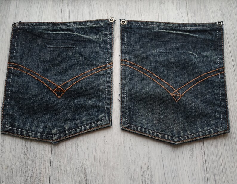 May include: Two dark blue denim pockets with brown stitching. The pockets have a diamond shape in the center and are sewn with a decorative stitch around the edges.