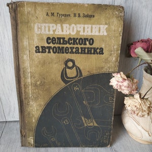 Puede incluir: Libro antiguo con una cubierta desgastada y texturizada. El título, en ruso, dice "Manual del mecánico rural". La portada presenta una ilustración en negro y dorado de llaves y una tuerca. El libro está ligeramente abierto, revelando sus páginas envejecidas.