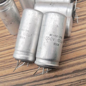 Puede incluir: Tres condensadores cilíndricos plateados con cables de alambre negros. Los condensadores tienen texto impreso, incluyendo "K50-356", "350V 100uF" y "9308".