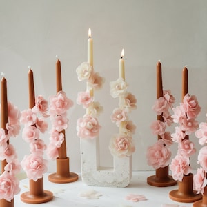 May include: A set of seven candle holders with white candles and pink flower accents. The candle holders are made of brown wood and have a simple design.