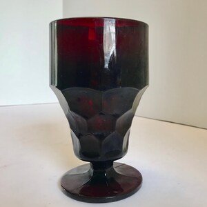 Puede incluir: Una copa de vidrio de color rojo oscuro con un diseño texturizado y un tallo corto.
