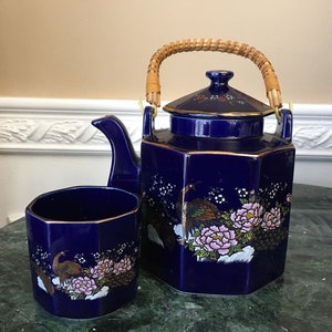 Peut inclure: Une théière bleu cobalt avec une poignée en osier et des accents dorés. La théière présente un motif floral et d'oiseaux. Une tasse à thé bleu cobalt assortie est également représentée.