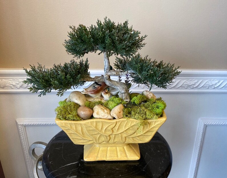 May include: A yellow ceramic planter with a leaf design, filled with green moss, small rocks, and a miniature bonsai tree with two ceramic birds.