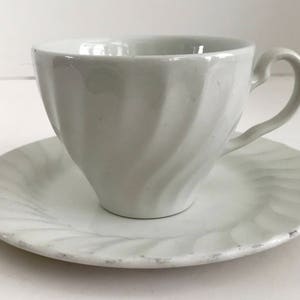 Puede incluir: Un juego de taza y platillo de té blanco con un diseño de espiral. La taza tiene un asa y el platillo tiene un borde festoneado.