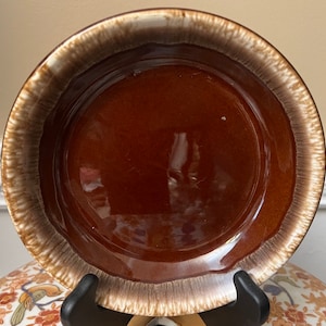 Peut inclure: Un bol en céramique brun avec un bord blanc. Le bol a une finition émaillée et est légèrement arrondi.