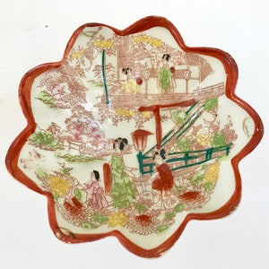 Puede incluir: Un cuenco de cerámica blanca con un borde rojo y un diseño floral. El cuenco presenta una escena de mujeres japonesas con ropa tradicional caminando por un jardín con una pagoda en el fondo.