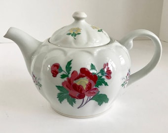 May include: White porcelain teapot with a floral design featuring red, yellow, and green flowers. The teapot has a lid and a handle.